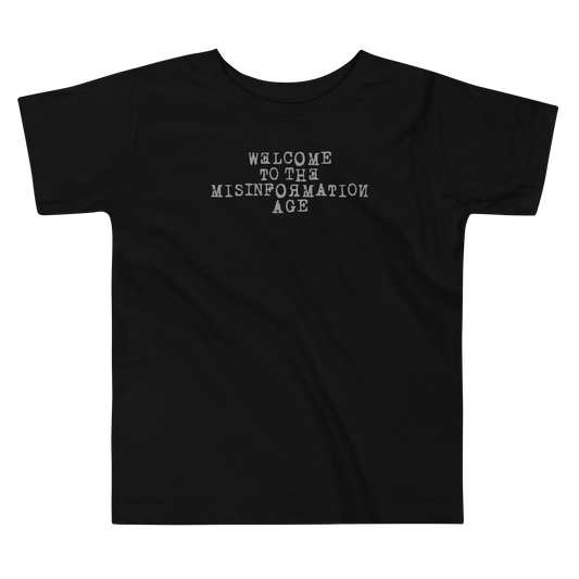 "Welcome to the misinformation age" printed on a black toddler short sleeve tee laying on a flat surface