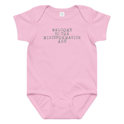 "Welcome to the misinformation age" printed on a pink baby jersey bodysuit laying on a flat surface amongst other clothes
