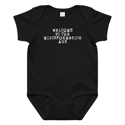 "Welcome to the misinformation age" printed on a black baby jersey bodysuit laying on a flat surface amongst other clothes