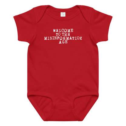 "Welcome to the misinformation age" printed on a red baby jersey bodysuit laying on a flat surface amongst other clothes