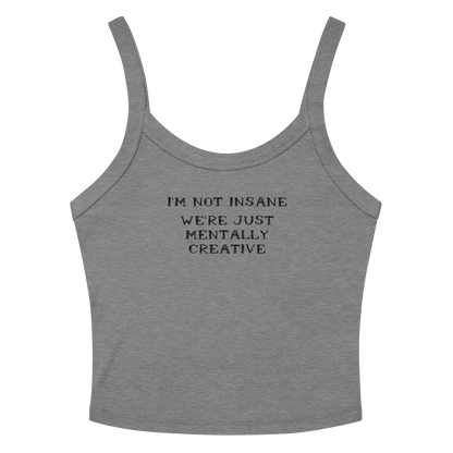 "I’m not insane   We’re just mentally creative" printed on a athletic heather women's micro-rib tanktop laying on a flat surface amongst sunglasses and shorts