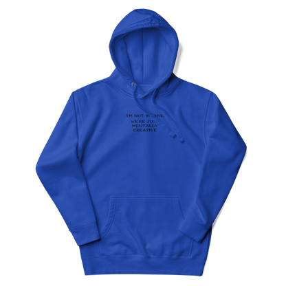 "I’m not insane   We’re just mentally creative" printed on a team royal unisex hoodie laying on a flat surface with the hood up