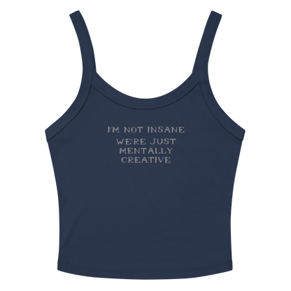 "I’m not insane   We’re just mentally creative" printed on a solid navy blend women's micro-rib tanktop laying on a flat surface amongst sunglasses and shorts