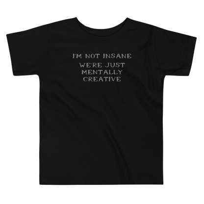 "I’m not insane   We’re just mentally creative" printed on a black toddler short sleeve tee laying on a flat surface