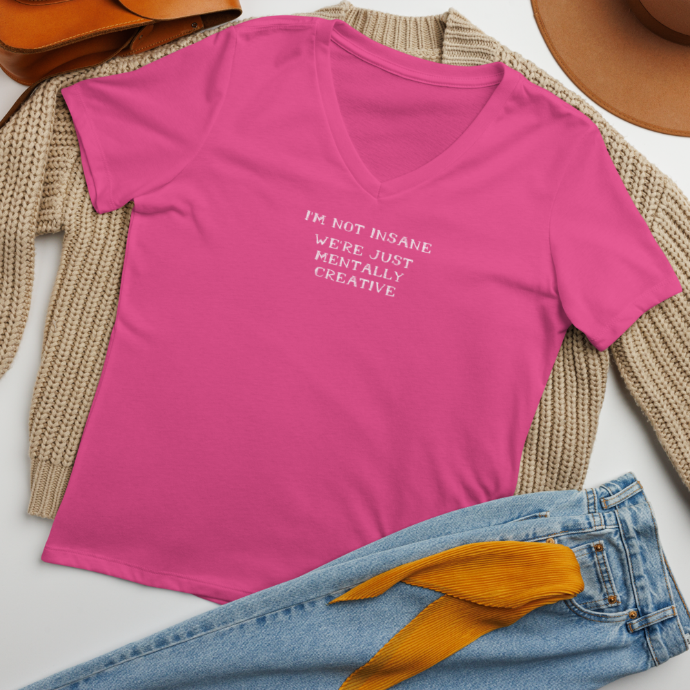 "I’m not insane   We’re just mentally creative" printed on a berry women's relaxed v-neck t-shirt laying on a flat surface amongst other clothes