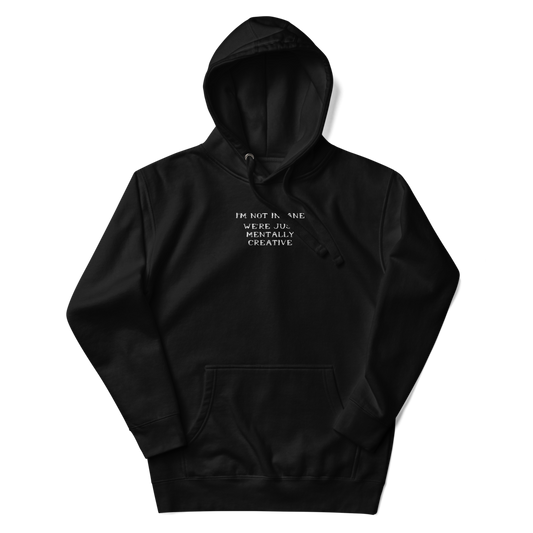 "I’m not insane   We’re just mentally creative" printed on a black unisex hoodie laying on a flat surface with the hood up