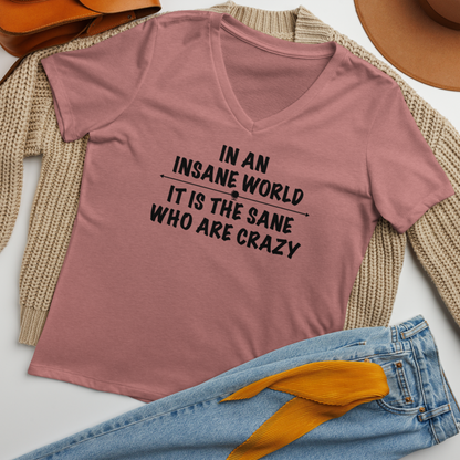 "In an insane world, it is the sane who are crazy" printed on a heather mauve women's relaxed v-neck t-shirt laying on a flat surface amongst other clothes