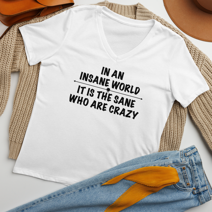 "In an insane world, it is the sane who are crazy" printed on a solid white blend women's relaxed v-neck t-shirt laying on a flat surface amongst other clothes