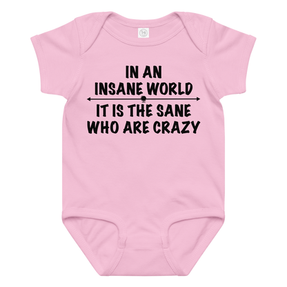 "In an insane world, it is the sane who are crazy" printed on a pink baby jersey bodysuit laying on a flat surface amongst other clothes
