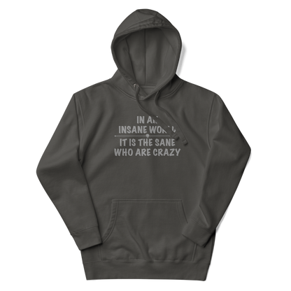 "In an insane world, it is the sane who are crazy" printed on a vintage black unisex hoodie laying on a flat surface with the hood up