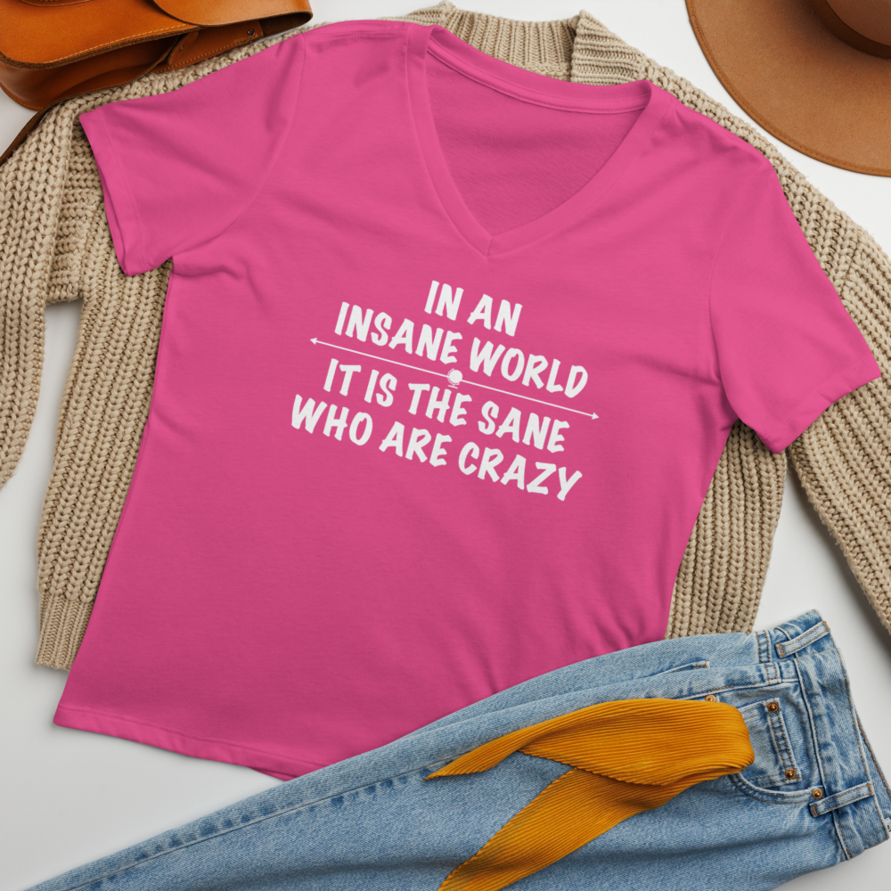 "In an insane world, it is the sane who are crazy" printed on a berry women's relaxed v-neck t-shirt laying on a flat surface amongst other clothes