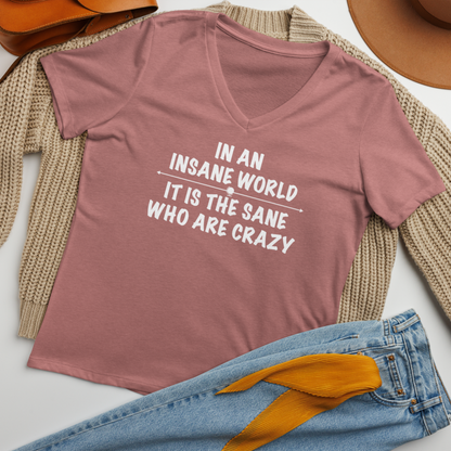 "In an insane world, it is the sane who are crazy" printed on a heather mauve women's relaxed v-neck t-shirt laying on a flat surface amongst other clothes