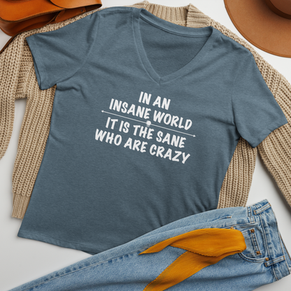 "In an insane world, it is the sane who are crazy" printed on a heather slate women's relaxed v-neck t-shirt laying on a flat surface amongst other clothes