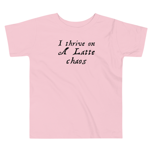 "I thrive on a latte chaos" printed on a pink toddler short sleeve tee laying on a flat surface