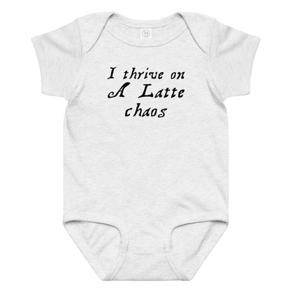 "I thrive on a latte chaos" printed on a ash baby jersey bodysuit laying on a flat surface amongst other clothes