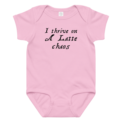 "I thrive on a latte chaos" printed on a pink baby jersey bodysuit laying on a flat surface amongst other clothes
