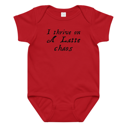"I thrive on a latte chaos" printed on a red baby jersey bodysuit laying on a flat surface amongst other clothes