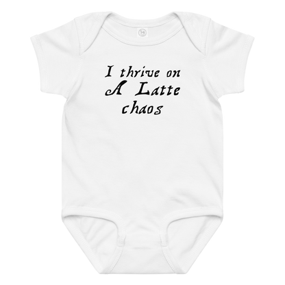 "I thrive on a latte chaos" printed on a white baby jersey bodysuit laying on a flat surface amongst other clothes