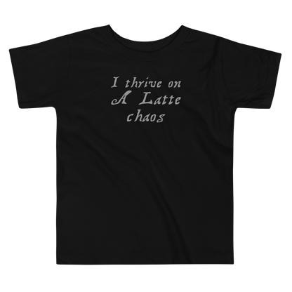 "I thrive on a latte chaos" printed on a black toddler short sleeve tee laying on a flat surface