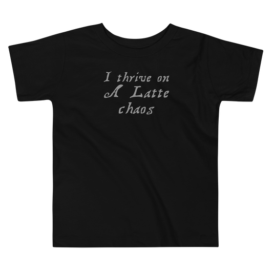 "I thrive on a latte chaos" printed on a black toddler short sleeve tee laying on a flat surface