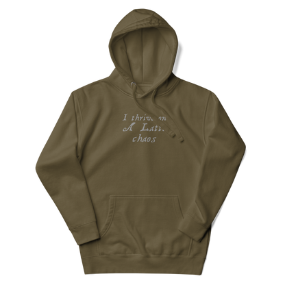 "I thrive on a latte chaos" printed on a military green unisex hoodie laying on a flat surface with the hood up