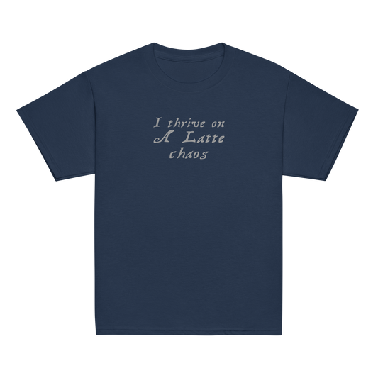 "I thrive on a latte chaos" printed on a navy youth classic tee laying on a flat surface