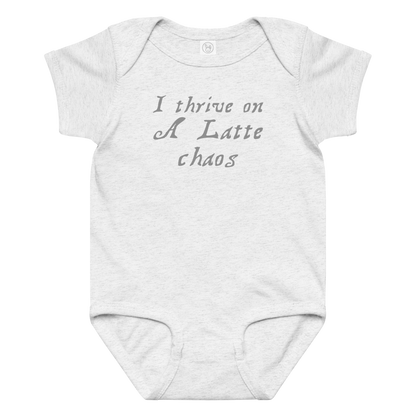 "I thrive on a latte chaos" printed on a ash baby jersey bodysuit laying on a flat surface amongst other clothes