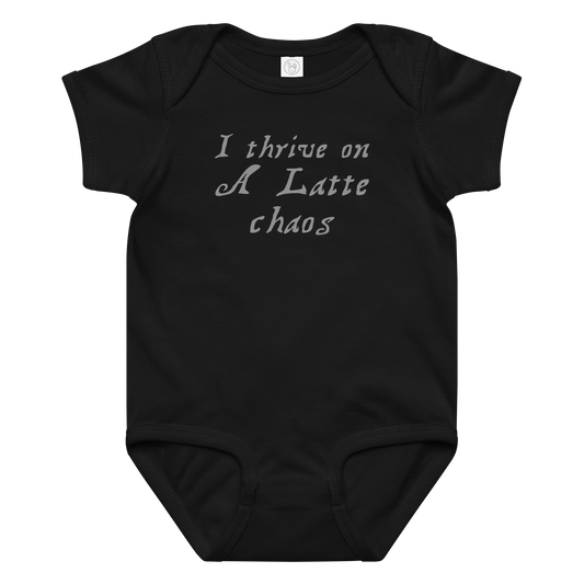 "I thrive on a latte chaos" printed on a black baby jersey bodysuit laying on a flat surface amongst other clothes