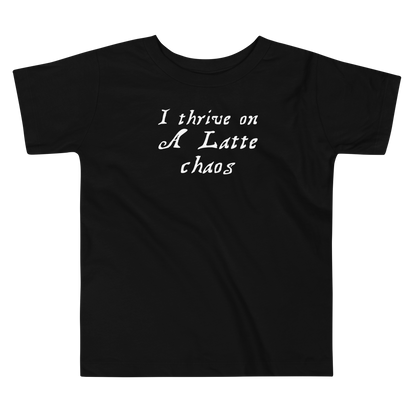 "I thrive on a latte chaos" printed on a black toddler short sleeve tee laying on a flat surface