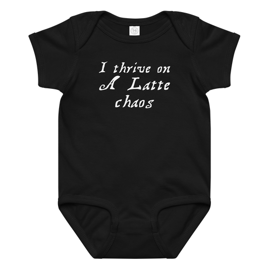 "I thrive on a latte chaos" printed on a black baby jersey bodysuit laying on a flat surface amongst other clothes