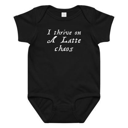 "I thrive on a latte chaos" printed on a black baby jersey bodysuit laying on a flat surface amongst other clothes