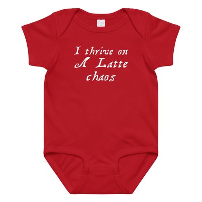 "I thrive on a latte chaos" printed on a red baby jersey bodysuit laying on a flat surface amongst other clothes