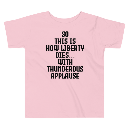 "So this is how liberty dies… with thunderous applause" printed on a pink toddler short sleeve tee laying on a flat surface