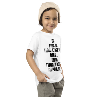 "So this is how liberty dies… with thunderous applause" printed on a white toddler short sleeve tee worn by a male who is also wearing a knit cap