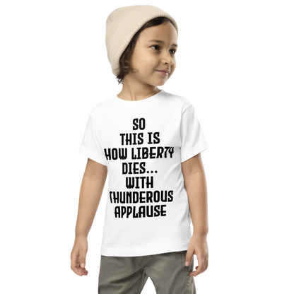 "So this is how liberty dies… with thunderous applause" printed on a white toddler short sleeve tee worn by a male wearing a cap