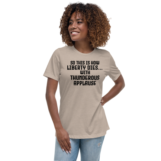 "So this is how liberty dies… with thunderous applause" printed on a heather stone women's relaxed t-shirt worn by a female
