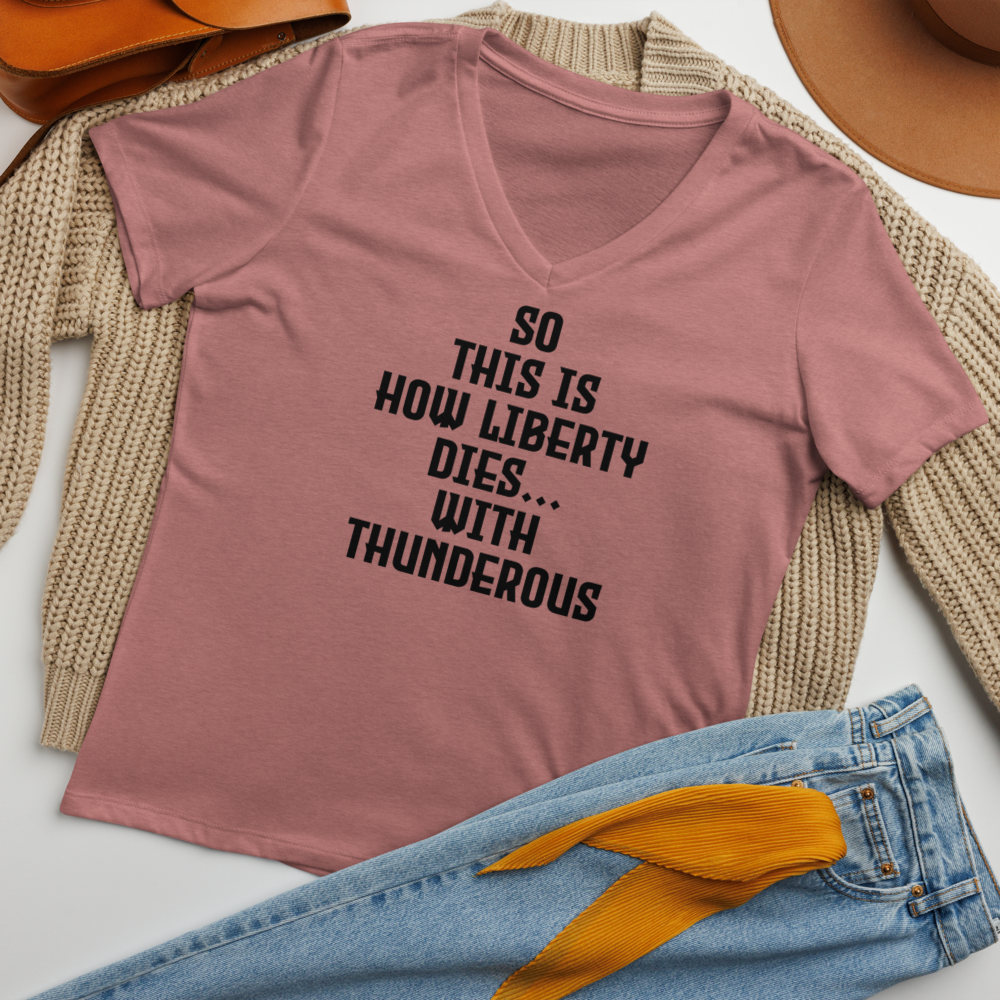 "So this is how liberty dies… with thunderous applause" printed on a heather mauve women's relaxed v-neck t-shirt laying on a flat surface amongst other clothes