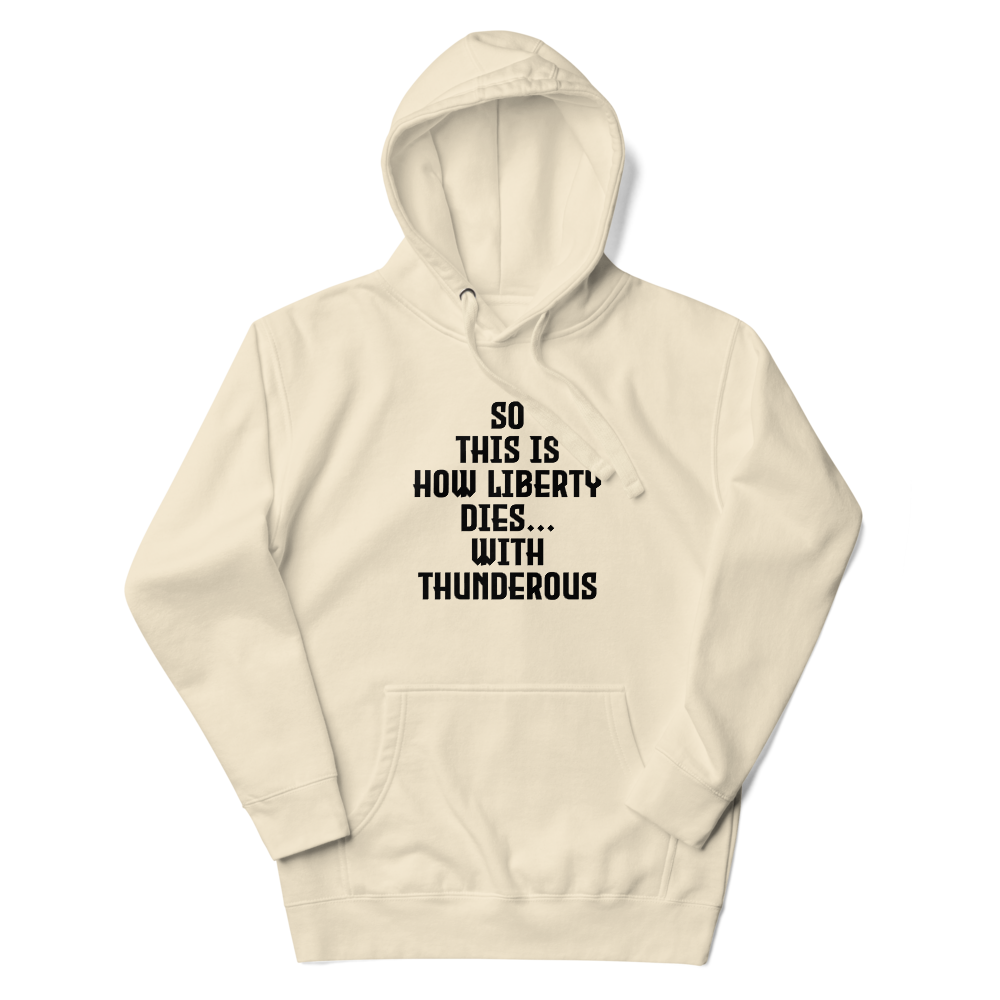 "So this is how liberty dies… with thunderous applause" printed on a bone unisex hoodie laying on a flat surface with the hood up