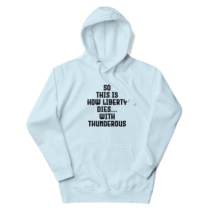 "So this is how liberty dies… with thunderous applause" printed on a sky blue unisex hoodie laying on a flat surface with the hood up