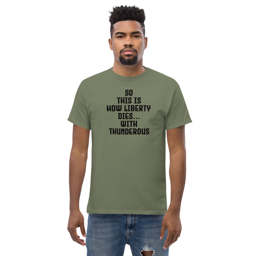 "So this is how liberty dies… with thunderous applause" printed on a military green unisex classic tee worn by a male