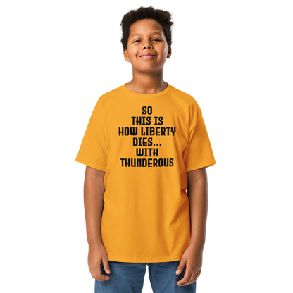 "So this is how liberty dies… with thunderous applause" printed on a gold youth classic tee worn by a male