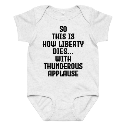 "So this is how liberty dies… with thunderous applause" printed on a ash baby jersey bodysuit laying on a flat surface amongst other clothes