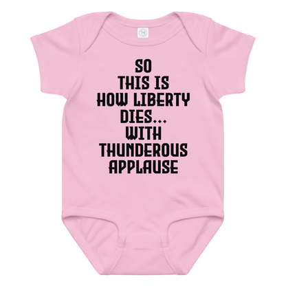 "So this is how liberty dies… with thunderous applause" printed on a pink baby jersey bodysuit laying on a flat surface amongst other clothes