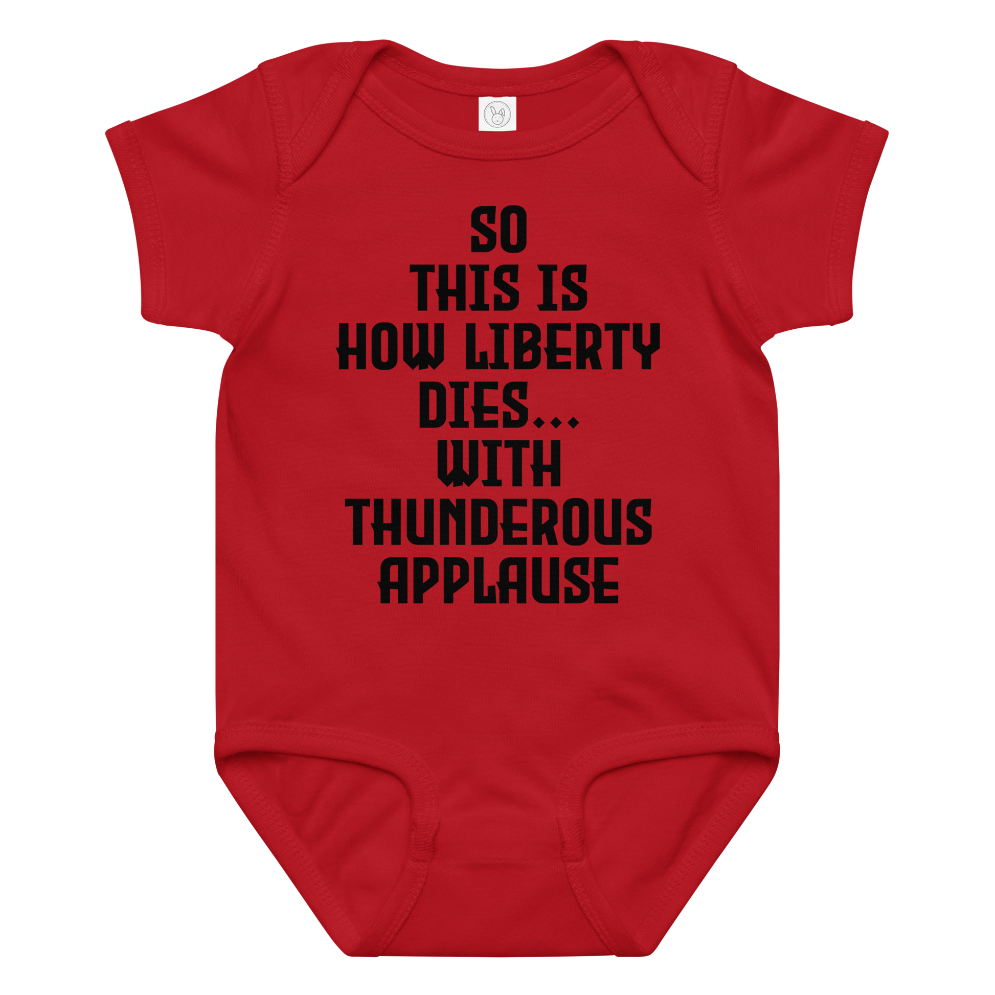 "So this is how liberty dies… with thunderous applause" printed on a red baby jersey bodysuit laying on a flat surface amongst other clothes