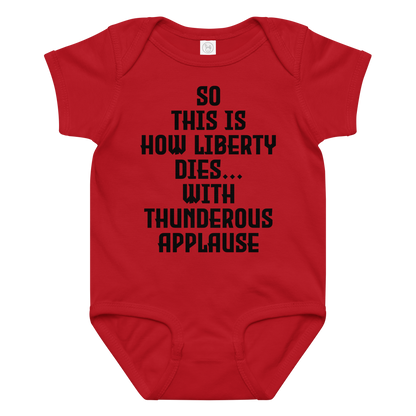 "So this is how liberty dies… with thunderous applause" printed on a red baby jersey bodysuit laying on a flat surface amongst other clothes