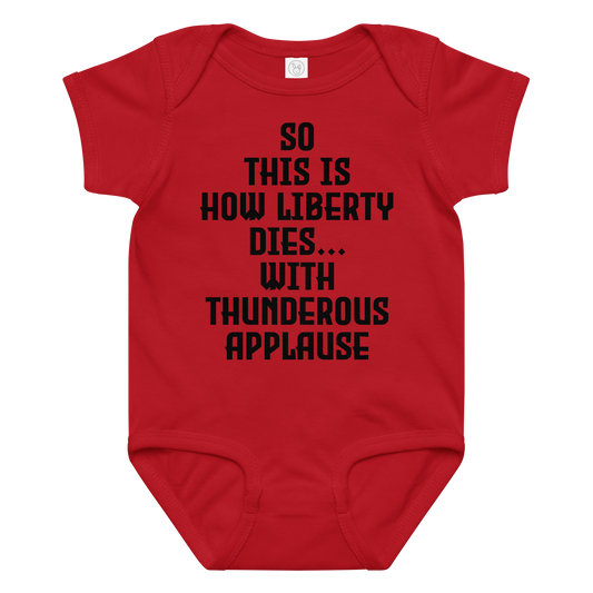 "So this is how liberty dies… with thunderous applause" printed on a red baby jersey bodysuit laying on a flat surface amongst other clothes