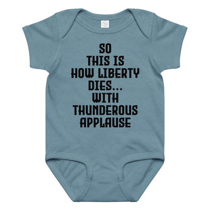 "So this is how liberty dies… with thunderous applause" printed on a vintage indigo baby jersey bodysuit laying on a flat surface amongst other clothes