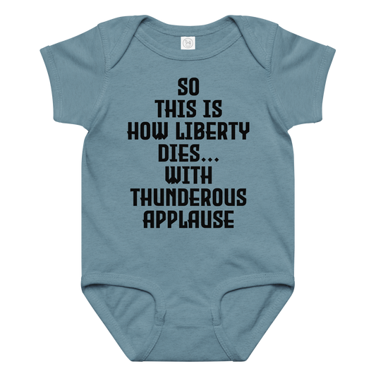 "So this is how liberty dies… with thunderous applause" printed on a vintage indigo baby jersey bodysuit laying on a flat surface amongst other clothes