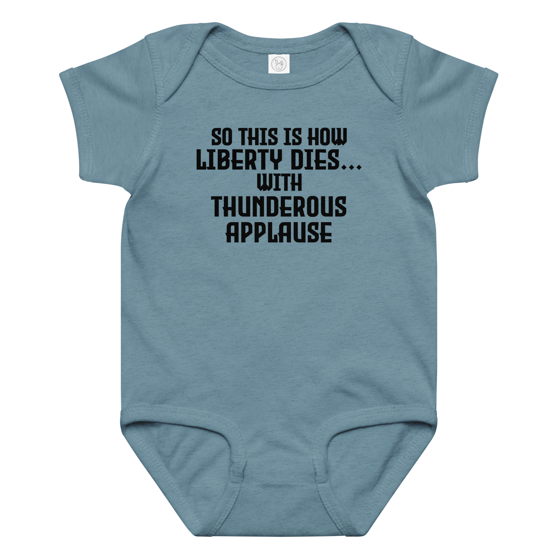 "So this is how liberty dies… with thunderous applause" printed on a vintage indigo baby jersey bodysuit laying on a flat surface amongst other clothes