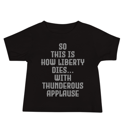 "So this is how liberty dies… with thunderous applause" printed on a black baby jersey short sleeve tee laying on a flat surface